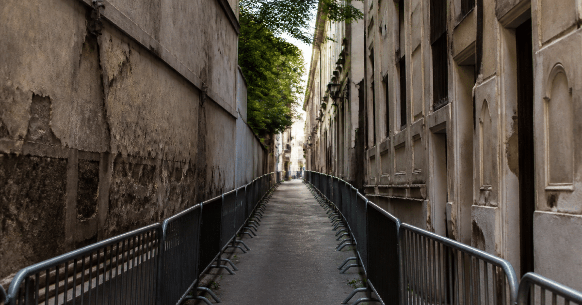 Rue étroite délimitée par bâtiments dégradés et barrières de sécurité