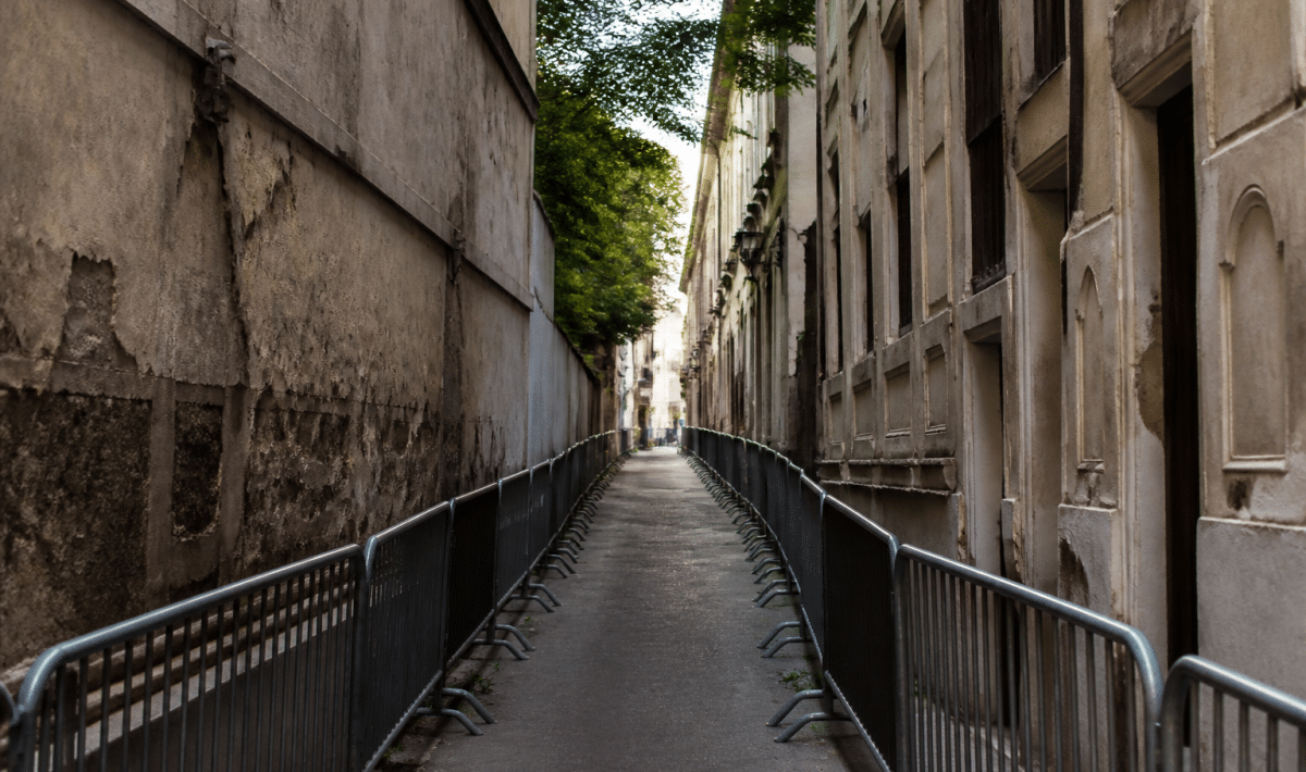 Rue étroite délimitée par bâtiments dégradés et barrières de sécurité