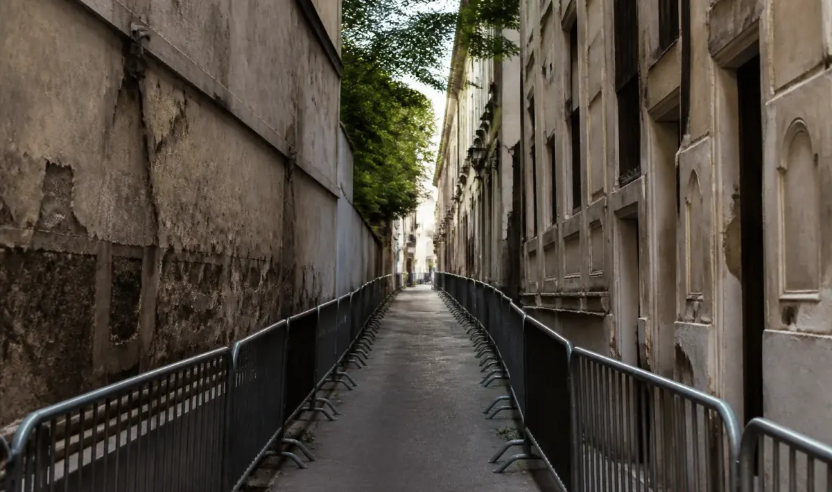 Rue étroite délimitée par bâtiments dégradés et barrières de sécurité