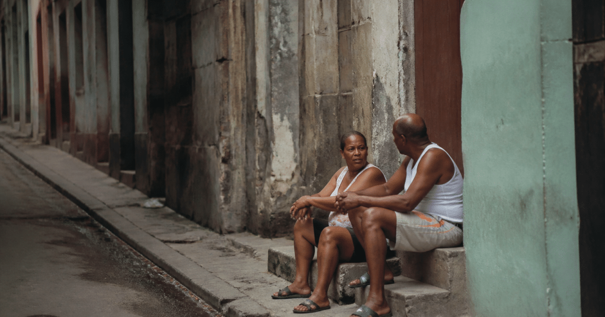 Rue sombre avec immeubles deteriores et habitants assis sur marches