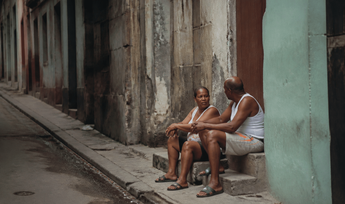 Rue sombre avec immeubles deteriores et habitants assis sur marches